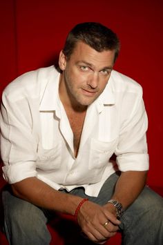 a man in white shirt sitting down with his hands on his knees and looking at the camera