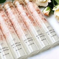 six personalized wedding favors in clear tubes with pink and white flowers on the side