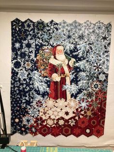 a quilted wall hanging with a santa clause holding a christmas tree and snowflakes