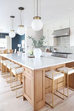 a large kitchen with white counter tops and gold barstool stools in front of an island