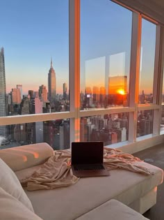 a laptop computer sitting on top of a white couch in front of a large window