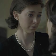 a woman wearing pearls is looking at another woman