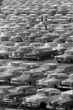 an old black and white photo of many cars in a parking lot with palm trees