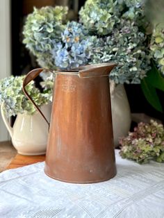 a brown pitcher sitting on top of a table next to some blue and green flowers