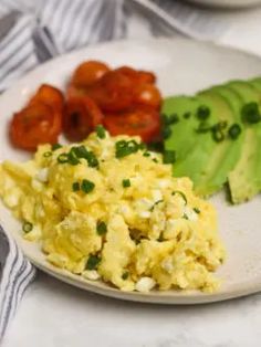 scrambled eggs, avocado and tomatoes on a white plate