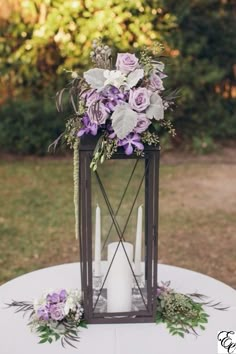 a candle holder with flowers and greenery is on top of a white table cloth