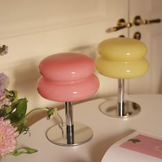 two vases sitting on top of a white table next to pink and yellow flowers