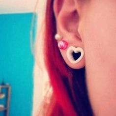 a woman with red hair is wearing ear piercings and has a heart on it