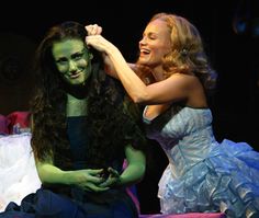 two people dressed in costumes on stage one is holding the other's hair and smiling