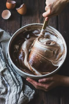 two hands holding a bowl filled with chocolate ice cream and an egg on the side