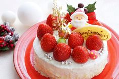 a christmas cake decorated with strawberries and santa clause on top, sitting on a red plate