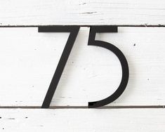 the number seven is placed on top of a white wooden wall with black metal numbers