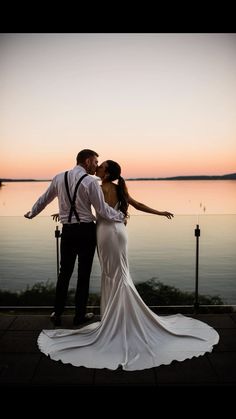 a bride and groom are kissing in front of the water at sunset on their wedding day