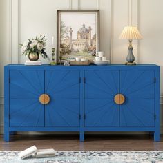 a blue sideboard with gold accents in a white living room, next to a painting and lamp