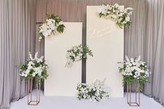 two white flowers and greenery are on display in front of a backdrop