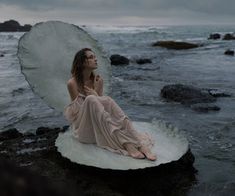 a woman sitting on top of a rock near the ocean