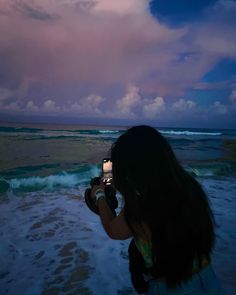 a woman taking a photo on the beach with her cell phone at sunset or dawn