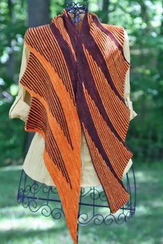 an orange and brown shawl is hanging on a rack in the grass near some trees