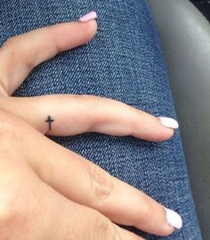 a person with pink fingernails and a cross tattoo on their finger, sitting in a car