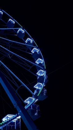 a ferris wheel lit up at night with lights on it's sides and in the dark