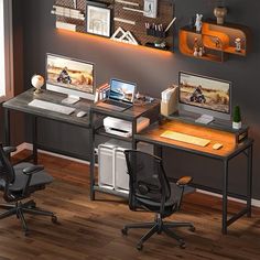 a desk with two computers on it in front of a gray wall and wooden floors