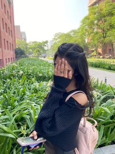 a woman is covering her face while sitting on a bench in front of some plants