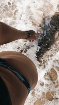 a woman standing on top of a beach next to the ocean with her feet in the water