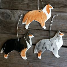 three ceramic dog ornaments hanging on a wooden surface with strings attached to them, one is orange and the other is white