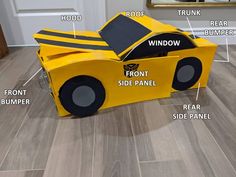 a cardboard car with parts labeled on the side and in front, sitting on top of a wood floor