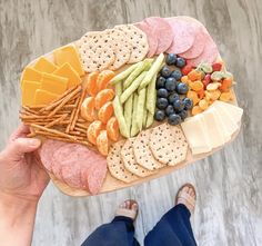 a person holding a platter with cheese, crackers, and fruit on it