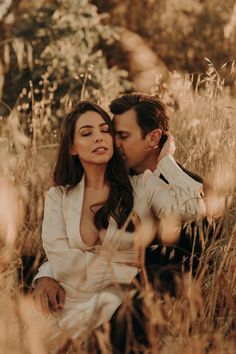 a man and woman are sitting in the tall grass with their heads close to each other