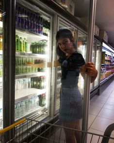 a woman standing in front of a refrigerator filled with water and sodas at night