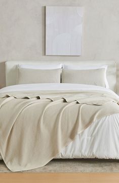 a bed with white sheets and pillows on top of it in a room next to a painting