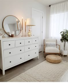 a bedroom with white furniture and a large round mirror on the wall above the dresser