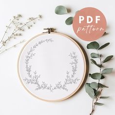 the embroidery pattern is being displayed next to some flowers and greenery on a white surface