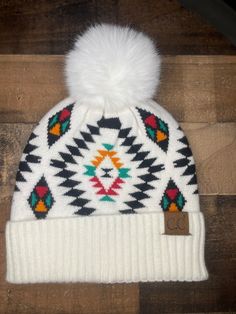 a white and black hat with a pom - pom on the top, sitting on a wooden floor