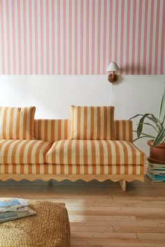 an orange and white striped couch sitting on top of a hard wood floor next to a potted plant