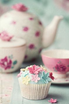 there is a cupcake with flowers on it next to a tea pot and saucer