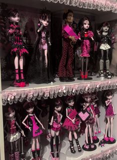 a shelf filled with lots of dolls in pink and black outfits on top of each other