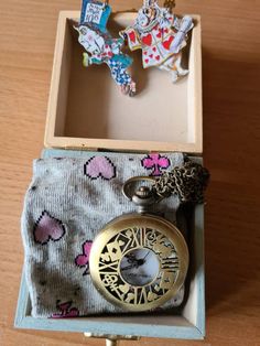 an open box with a pocket watch inside on a wooden table next to other items