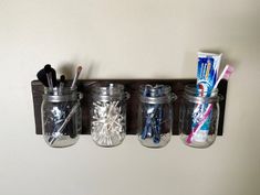 three mason jars with toothbrushes and toothpaste are hanging on the wall