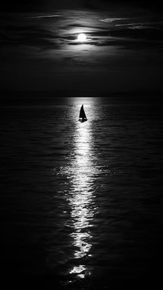 a black and white photo of a sailboat in the ocean at night with full moon