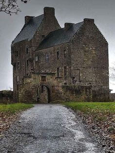 an old castle with a path leading to it in the middle of fall leaves on the ground