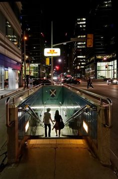 two people are walking up an escalator in the middle of a city at night