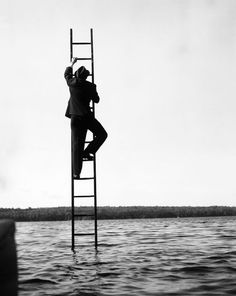 a man standing on top of a ladder next to a body of water