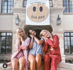 three women are sitting on a bench in front of a building with a sign that says, no sleep till biday