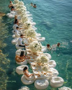 several people are swimming in the water with white floats and flowers on them, while others float