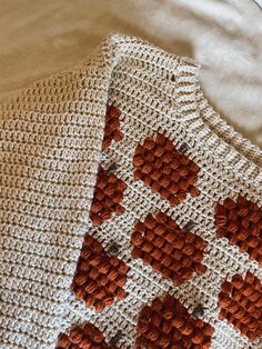 an orange and white knitted sweater laying on top of a bed next to a pillow