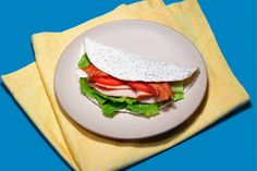 a white plate topped with a sandwich on top of a yellow napkin next to a blue background