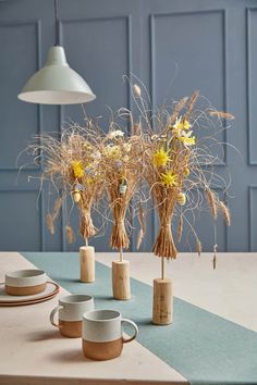 three vases with dried flowers in them sitting on a table next to plates and cups